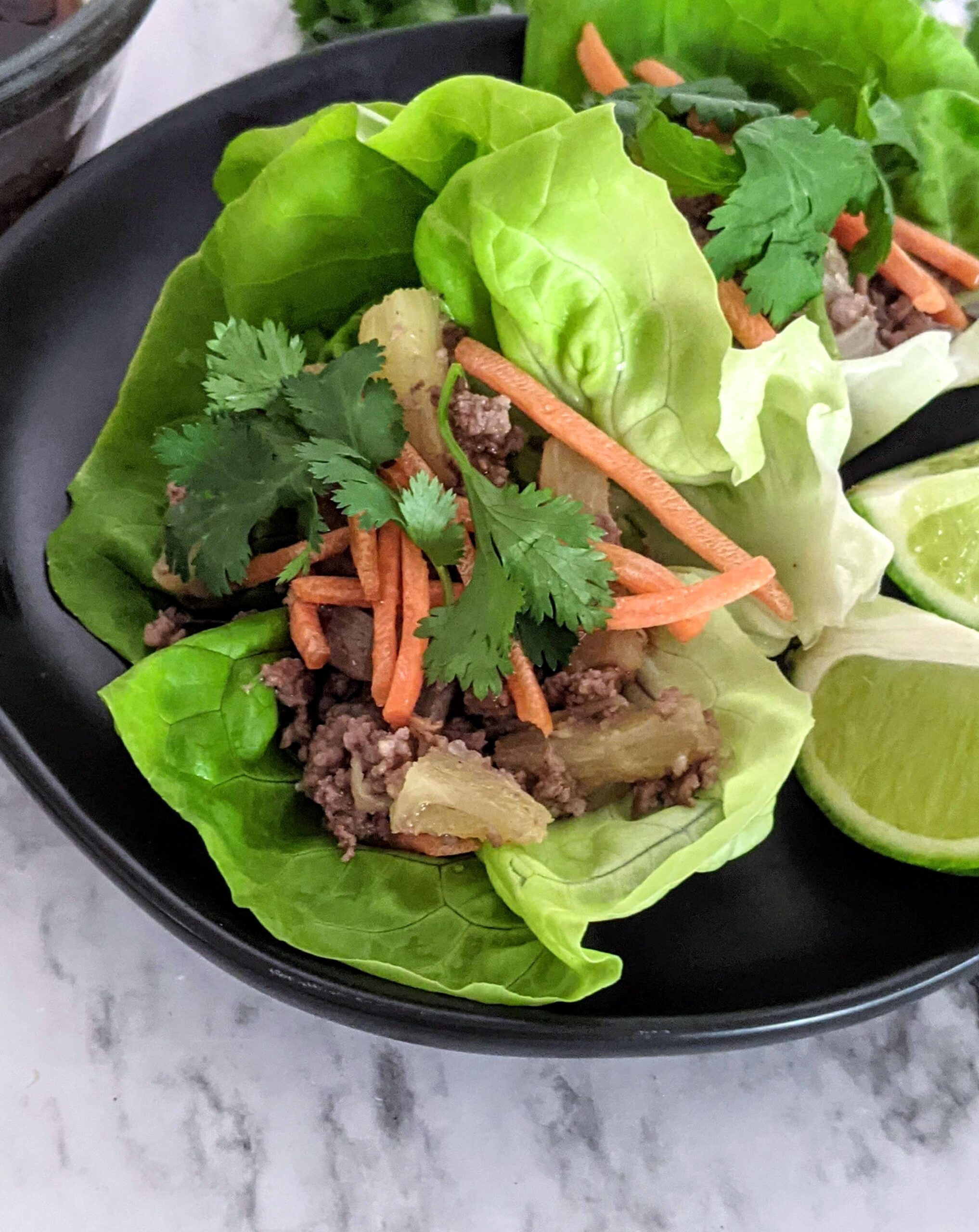 Lettuce wraps filled with pineapple beef sitting on a black plate.