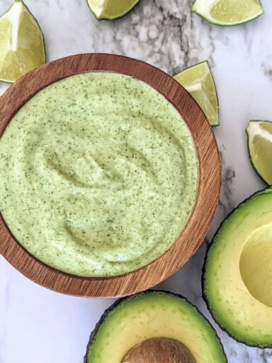 Bowl of cilantro lime dressing surrounded by avocado and lime wedges