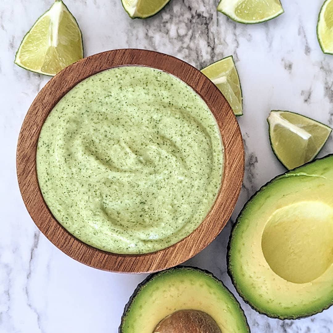Bowl of cilantro lime dressing surrounded by avocado and lime wedges