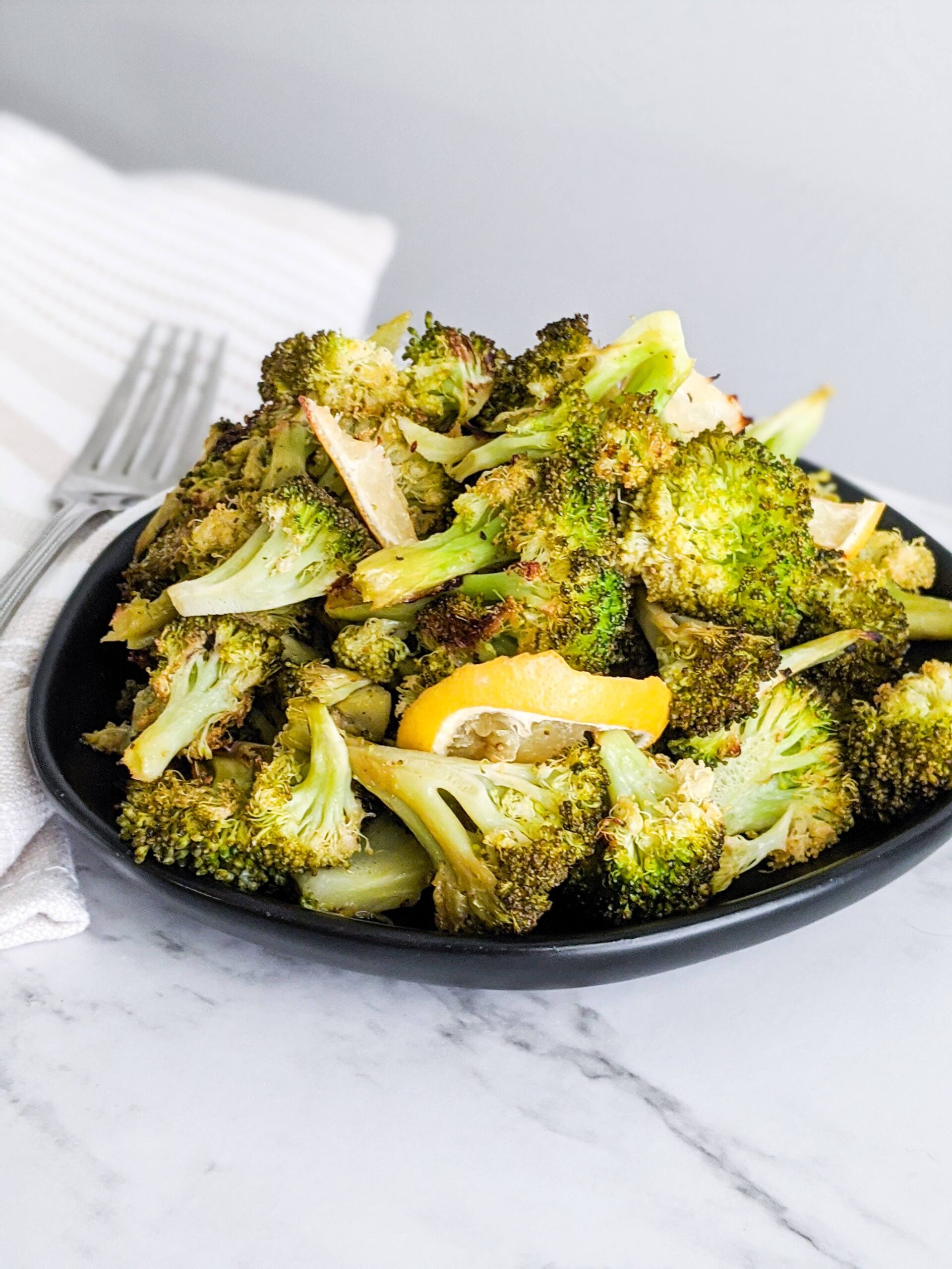 Black plate with roasted broccoli in a pile on top.