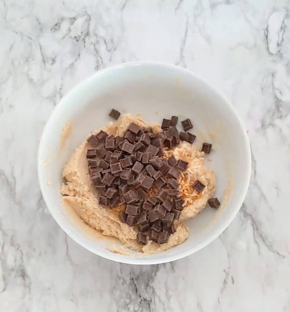 Bowl of cookie dough with coconut and chocolate chips ready to be mixed in. 