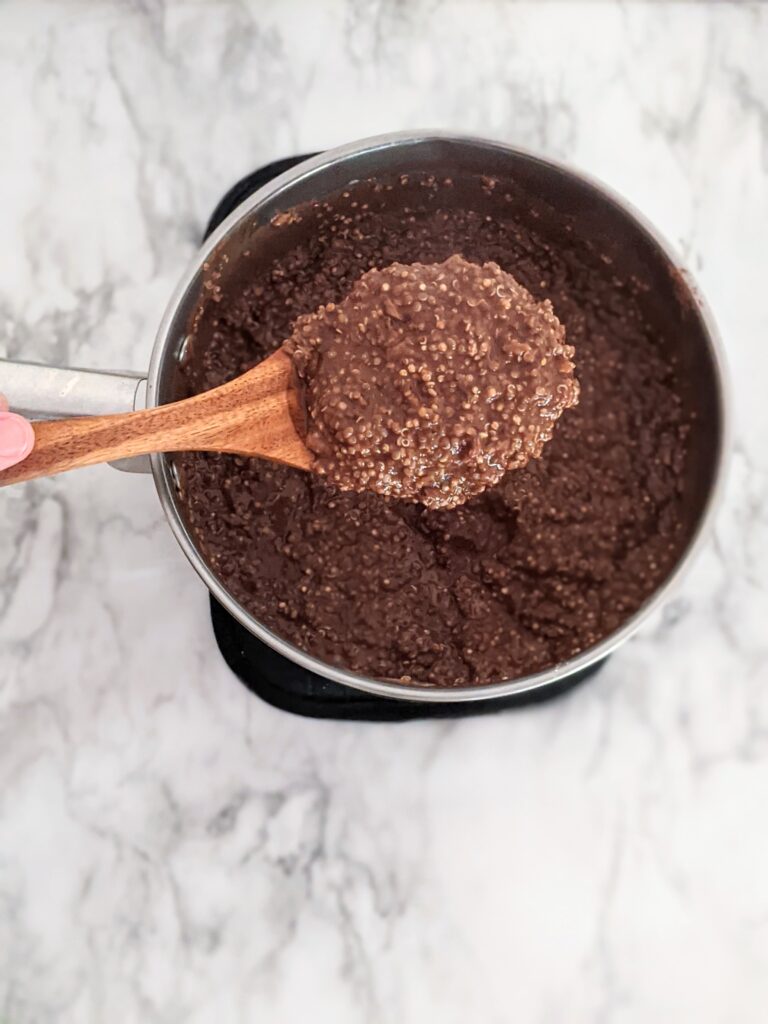Wooden spoon holding chocolate zucchini quinoa above a pot.
