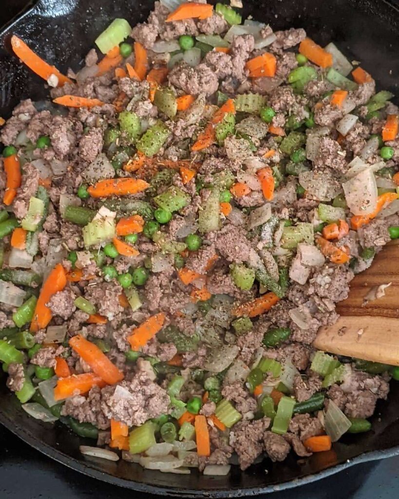 Cast iron skillet with meat and veggies cooking. 