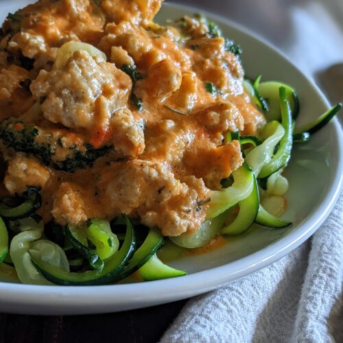 Plate of zucchini noodles topped with sausage and veggies in a red pepper sauce.