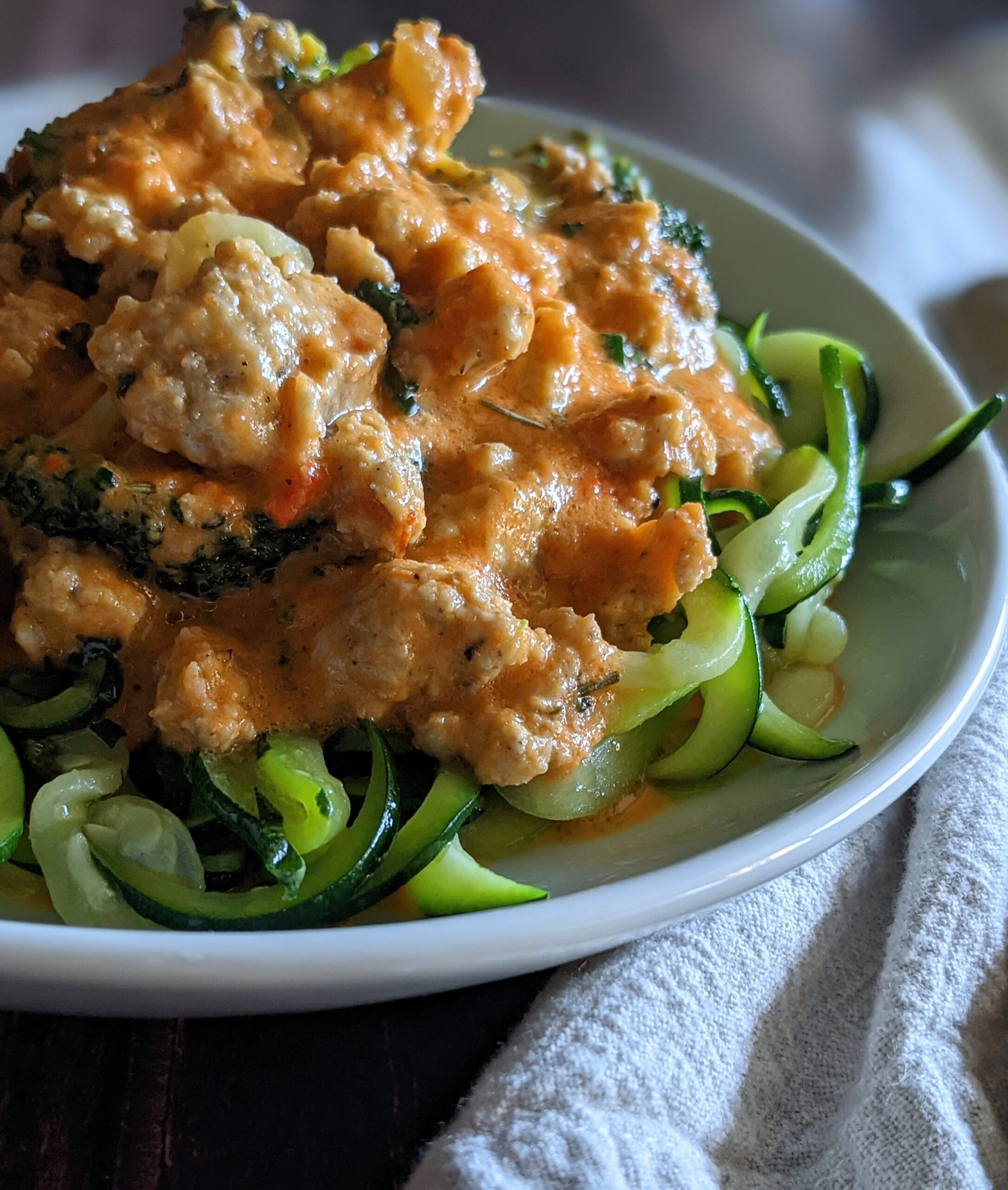 Plate of zucchini noodles topped with sausage and veggies in a red pepper sauce.
