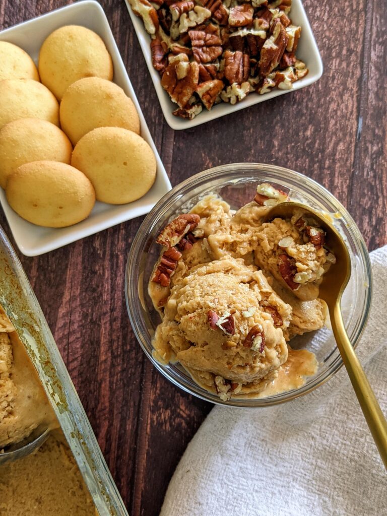 Glass cup of pumpkin nice cream surrounded by vanilla wafer cookies and chopped pecans. 