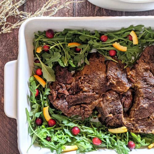 Half casserole dish of braised beef, surrounded by arugula with cranberries and orange peel.