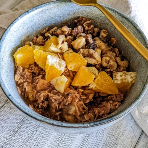 Bowl of chocolate orange oatmeal, topped with chopped walnuts and diced oranges. A gold spoon is laying diagonally across the top of the blue bowl.