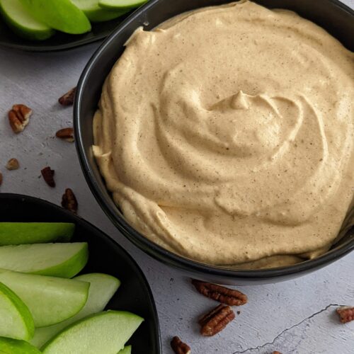 Black bowl of pumpkin dip with a plate of sliced green apples on the side.