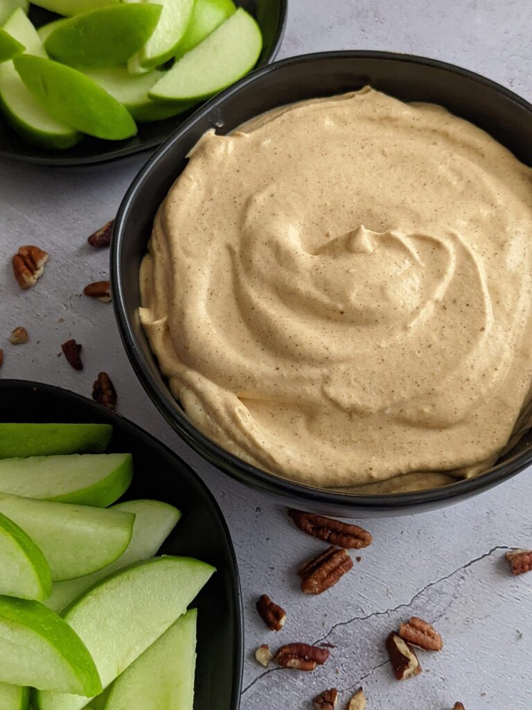 Black bowl of pumpkin dip with a plate of sliced green apples on the side.