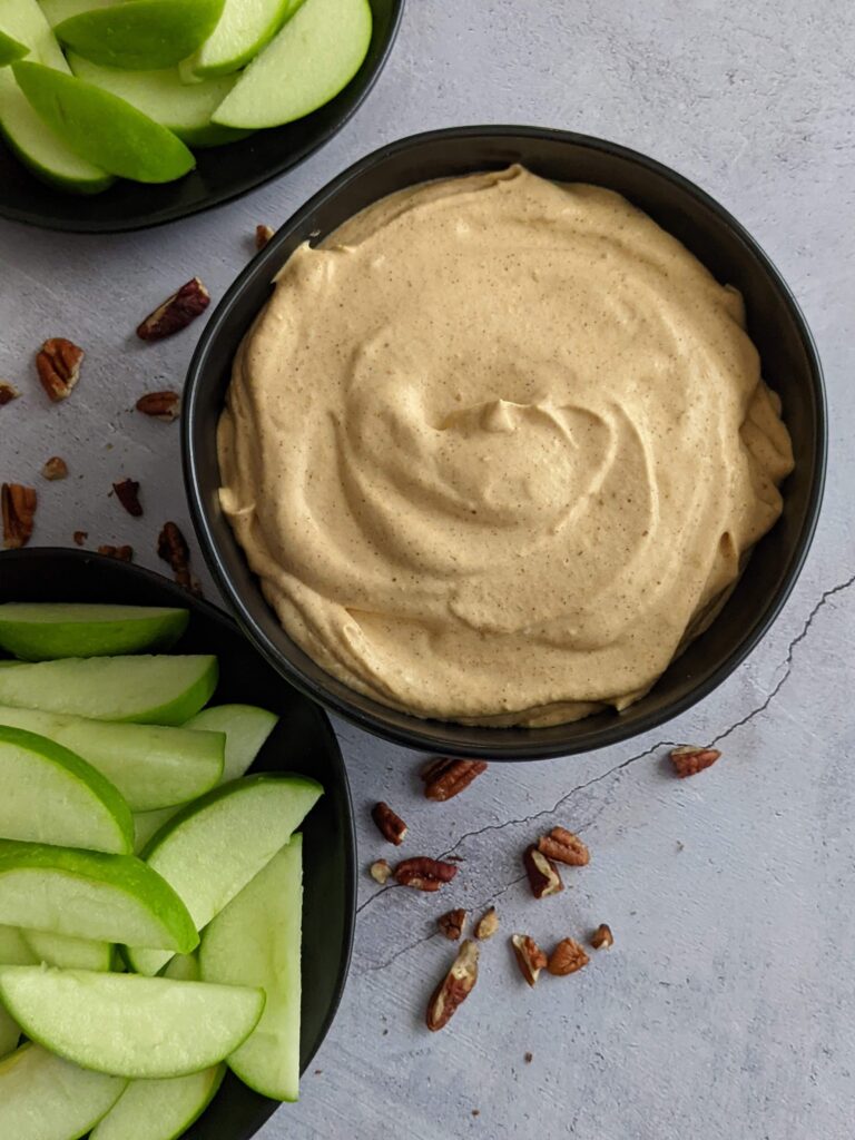 Black bowl of pumpkin dip with a plate of sliced green apples on the side.