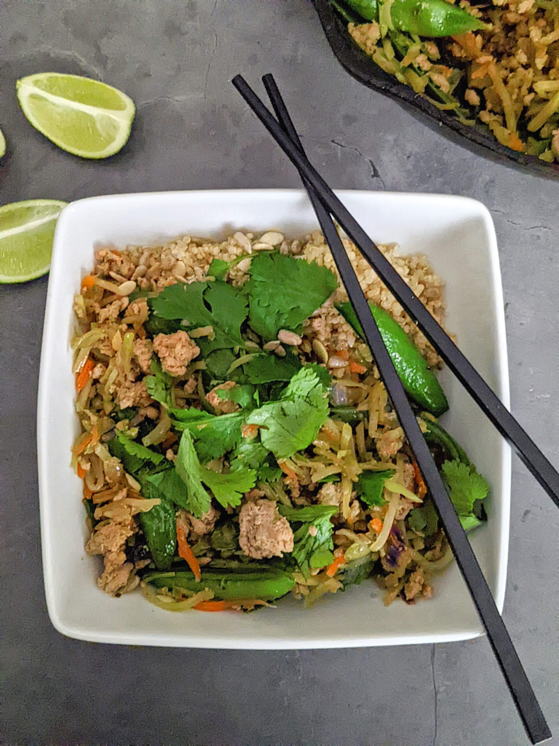 White square bowl with stir fry. Black chopsticks lay crossed on top of the bowl.