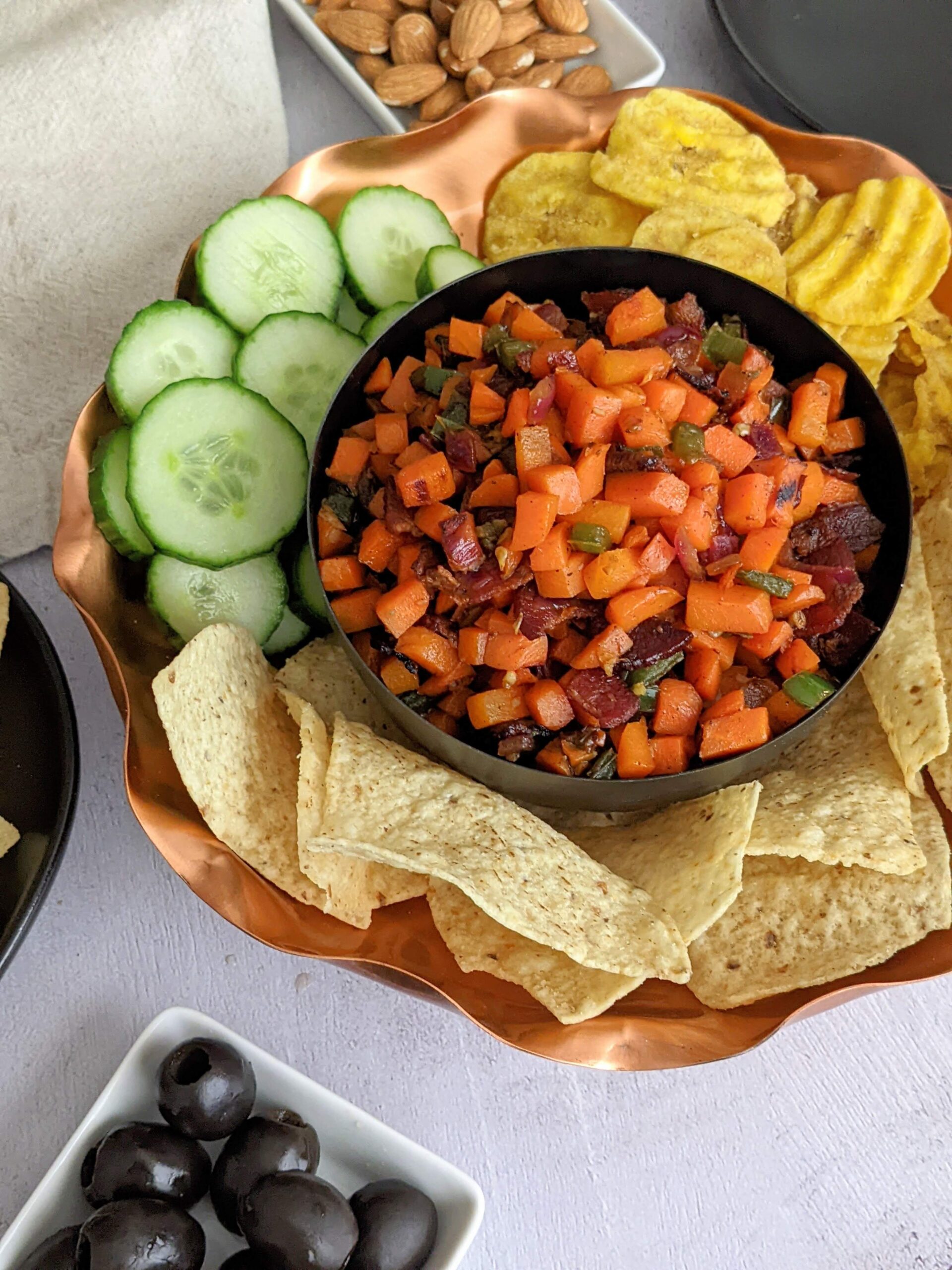 Copper serving bowl with carrot caviar in the middle surrounded by chips and cucumbers
