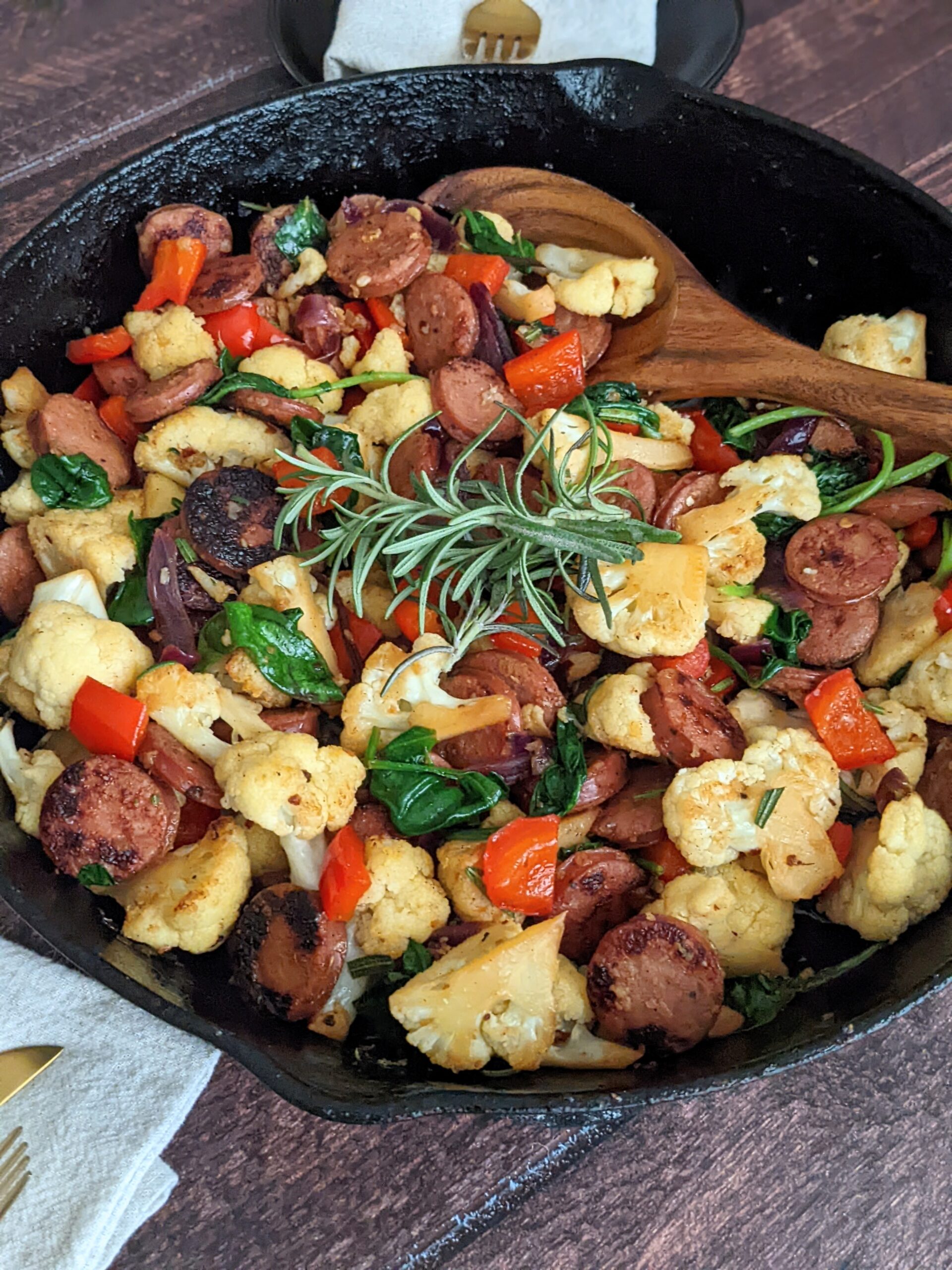 Cast iron skillet filled with sausage and veggie mixture and adorned with a sprig of rosemary.