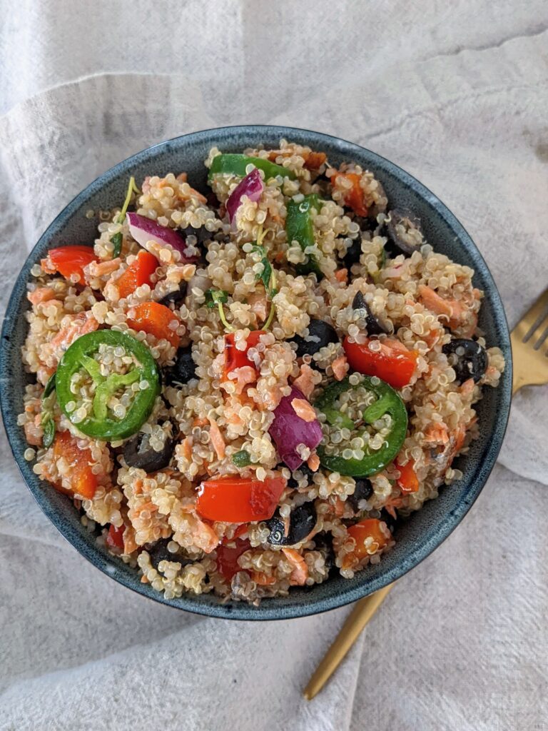 Top view of the blue bowl of salmon escabeche quinoa salad. It sits on a tan napkin with gold fork next to it. 