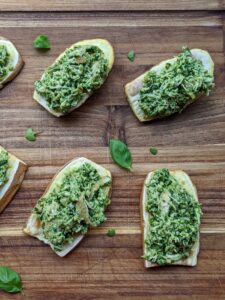 Slices of sweet potato chicken pesto toast on a wood cutting board with pieces of basil scattered around.