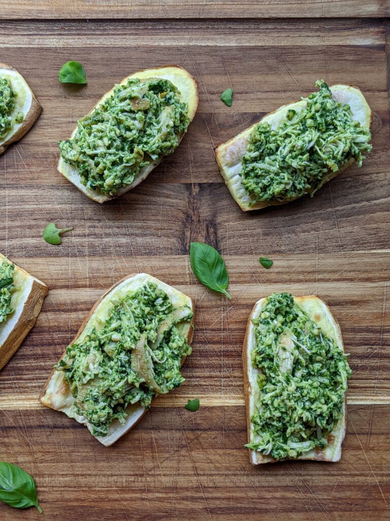 Slices of sweet potato chicken pesto toast on a wood cutting board with pieces of basil scattered around.
