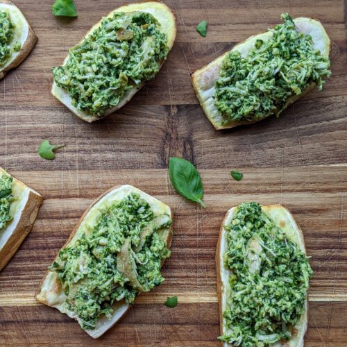 Slices of sweet potato chicken pesto toast on a wood cutting board with pieces of basil scattered around.