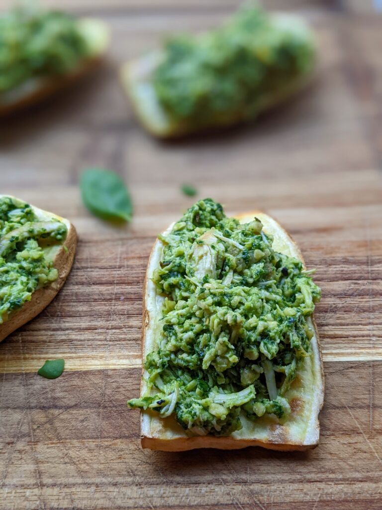 Closeup of a piece of sweet potato toast, topped with chicken tossed in pesto.
