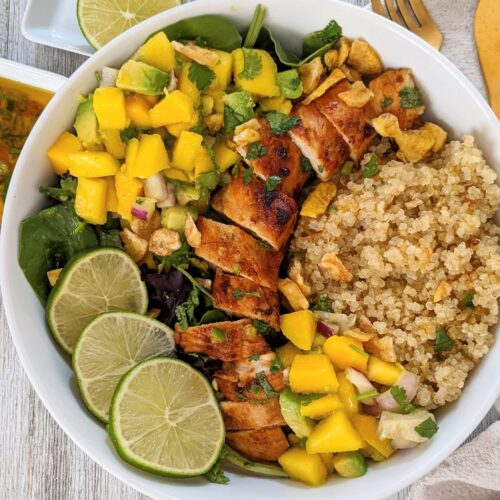 Top view of the mango and chicken taco bowl. The bowl is white, there are gold utensils on the side, and small side plates with leftover dressing and halved limes.