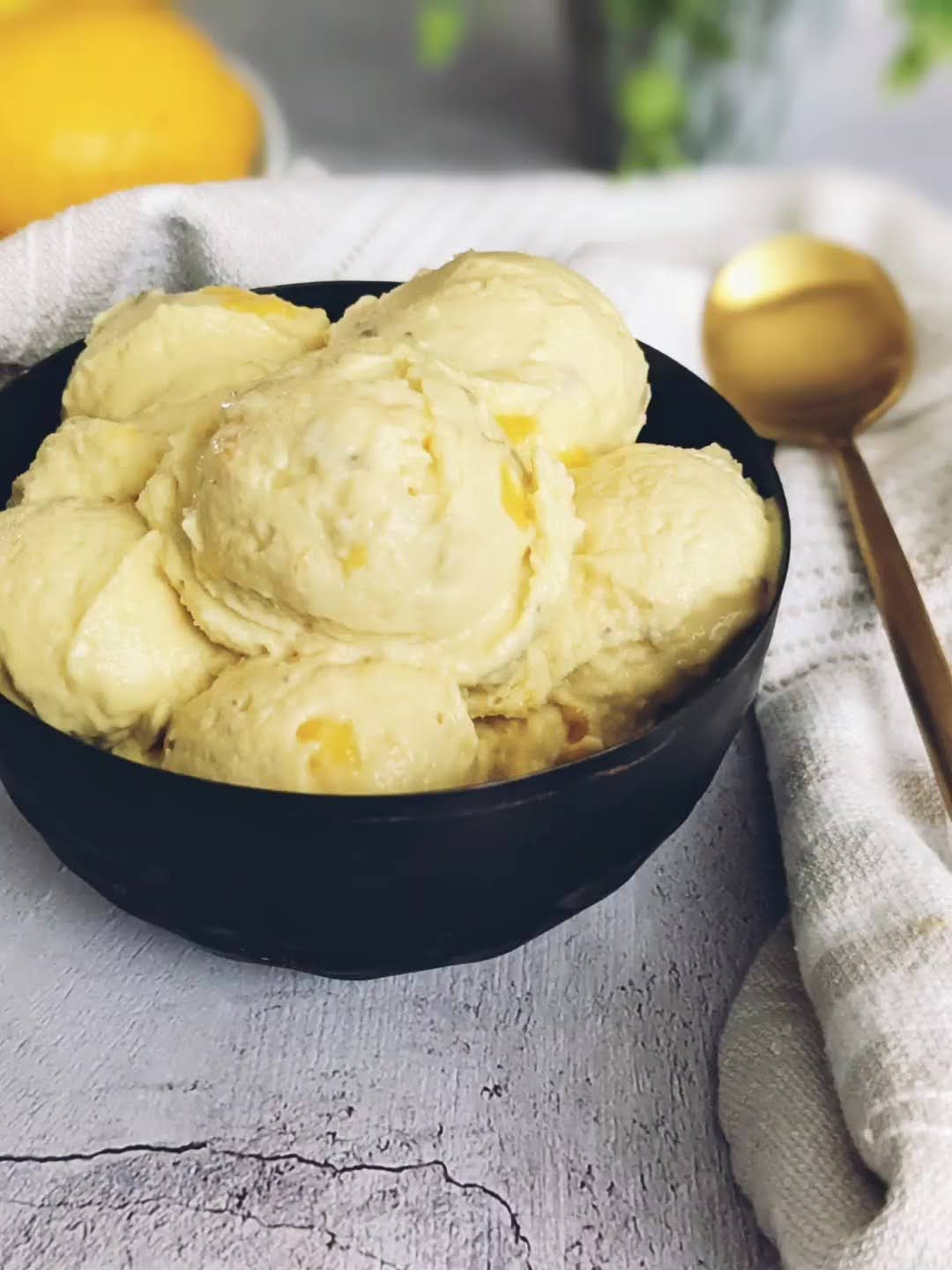 Small black bowl with scoops of mango banana nice cream. A gold spoon lays on a tan cloth napkin next to the bowl.