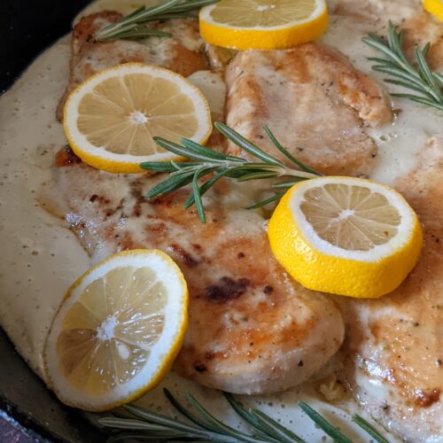 An angled view of a cast iron pan holding the creamy lemon and rosemary chicken.
