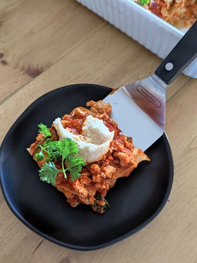 A metal spatula serving a slice of lasagna on a black plate.