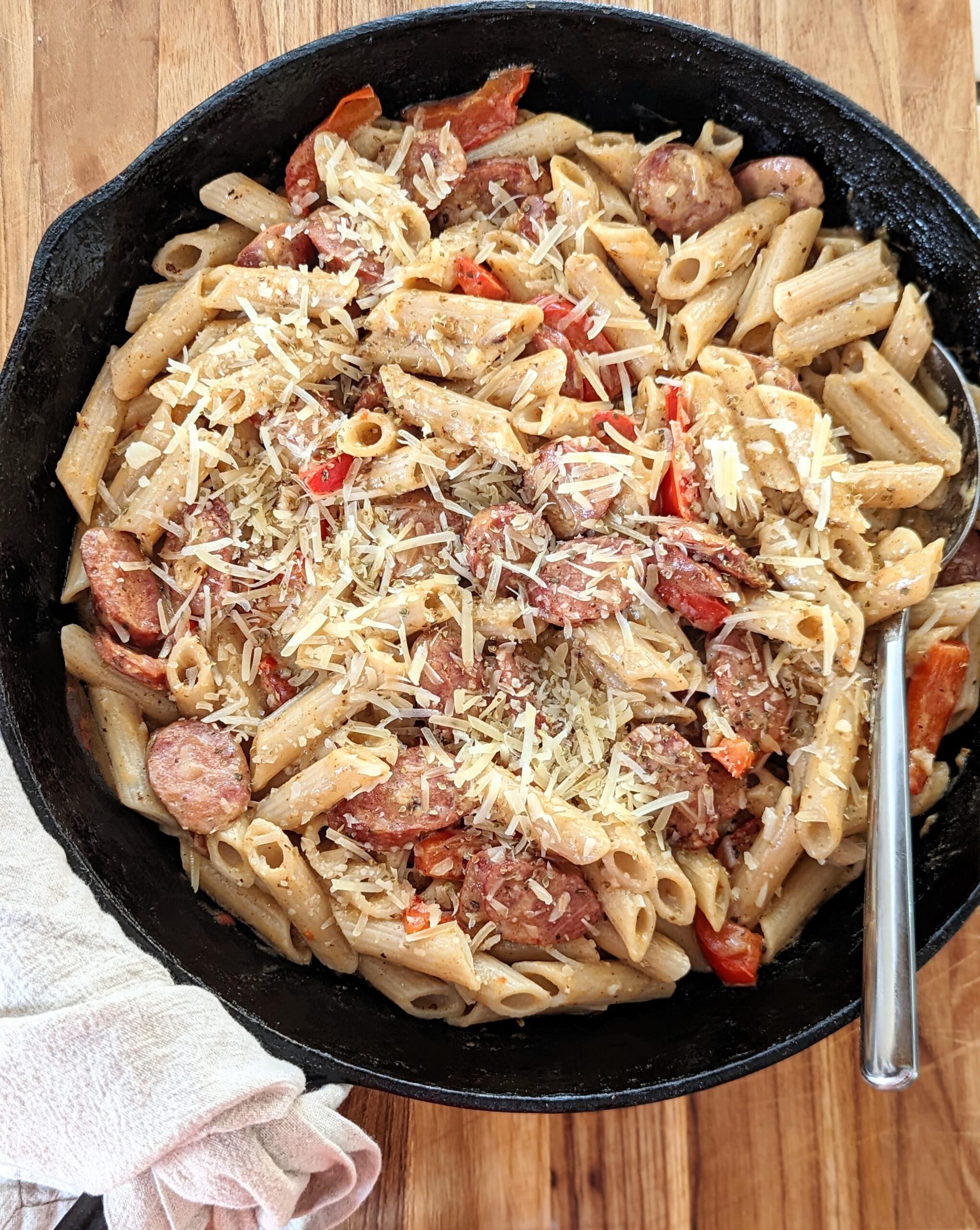 Top view of a cast iron skillet filled with Cajun Pasta. A silver spoon sits in the pasta, and a towel is wrapped around the handle of the skillet.