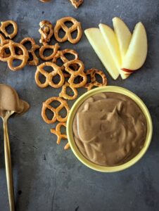 Overhead shot of the cinnamon dip in a yellow ramekin, surrounded by apple slices and mini pretzels.
