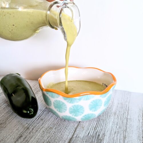 The vinaigrette is being poured from the glass bottle into a measuring cup.