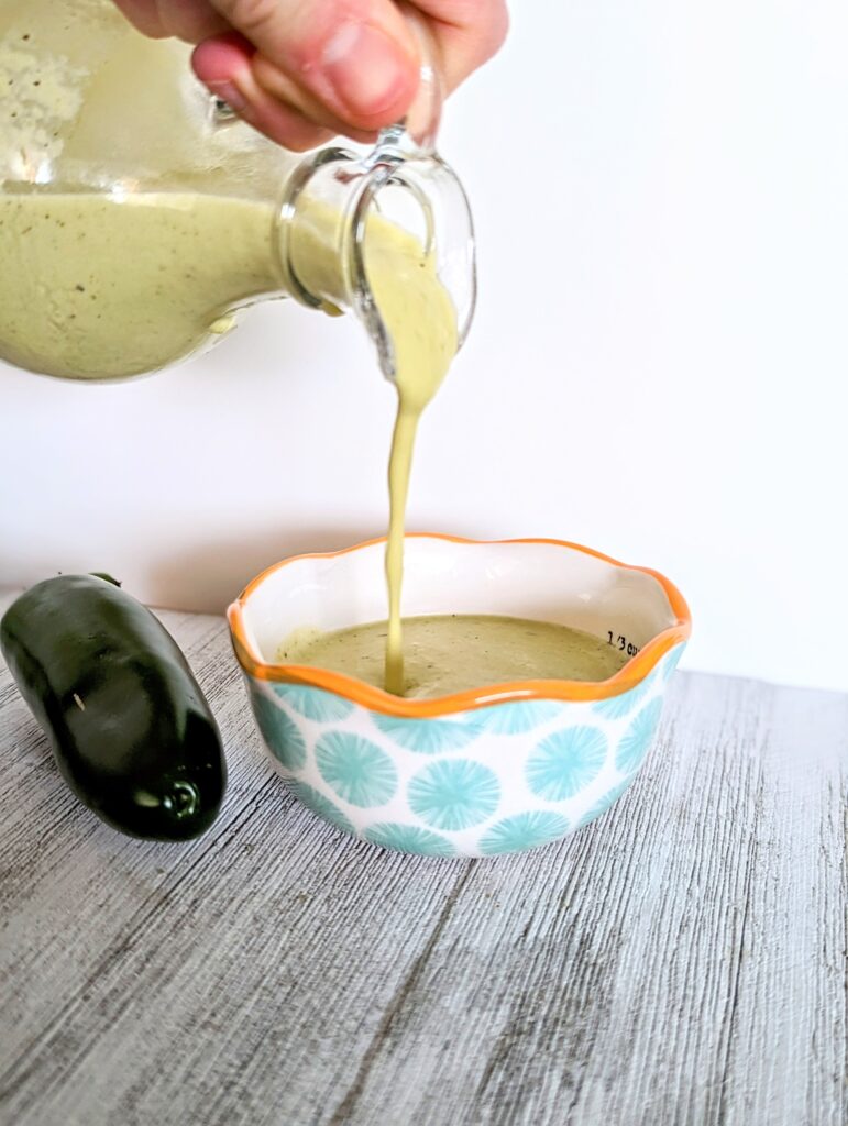 The vinaigrette is being poured from the glass bottle into a measuring cup.