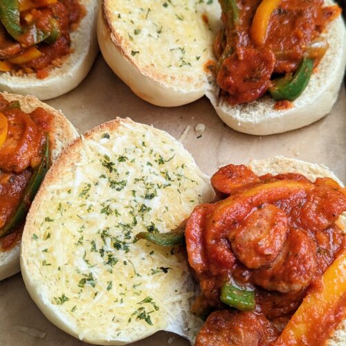 Closeup of the sausage and pepper sandwiches laid out on a baking tray. The sandwiches lie open.