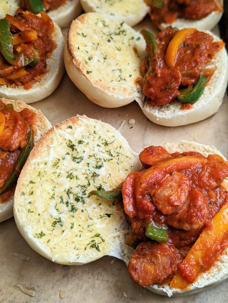 Closeup of the sausage and pepper sandwiches laid out on a baking tray. The sandwiches lie open. 